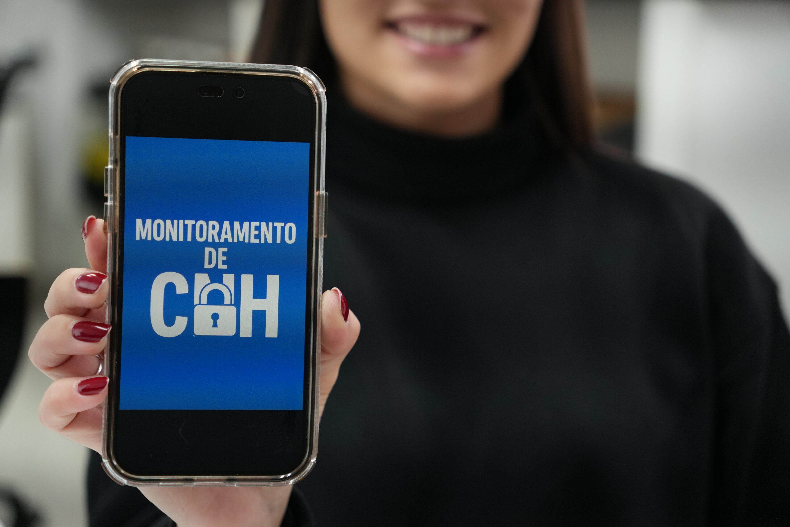 Mulher segurando celular com o aplicativo de monitoramento de CNH na tela, representando como evitar a suspensão da carteira de habilitação com ajuda profissional.