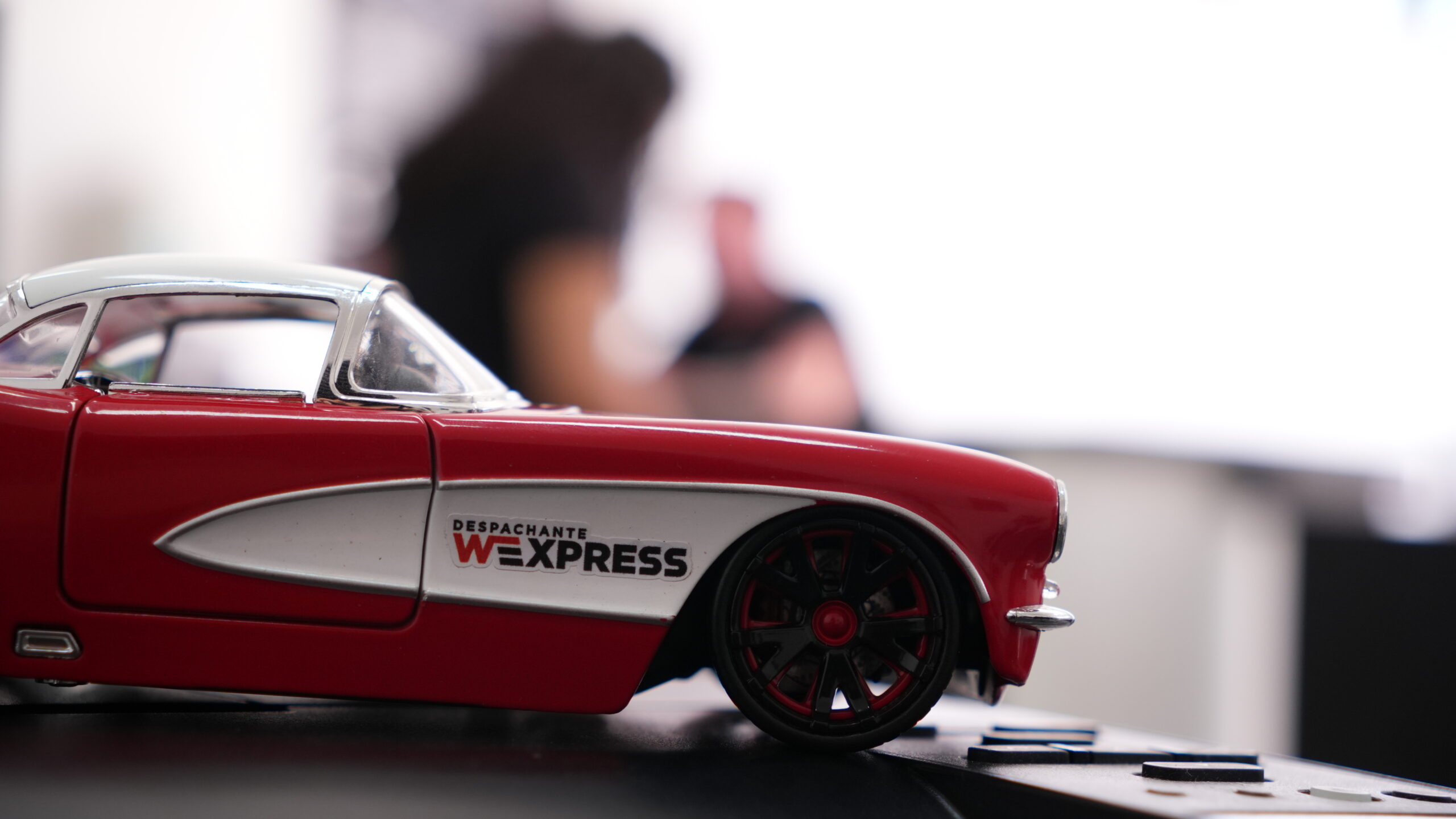 miniatura de carro do WExpress com funcionria ao fundo verificando licenciamento